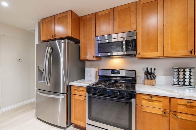 kitchen with light hardwood / wood-style floors, light stone counters, and stainless steel appliances