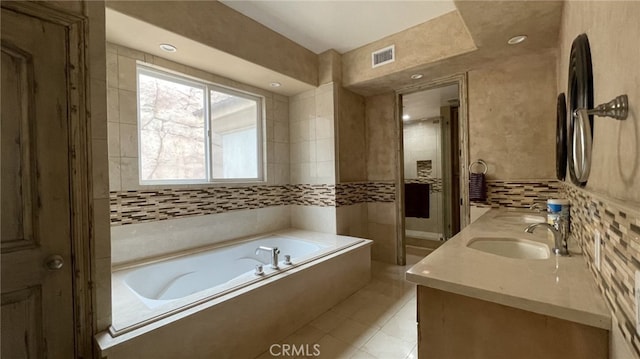 bathroom with tile floors, vanity with extensive cabinet space, a bath to relax in, and tile walls