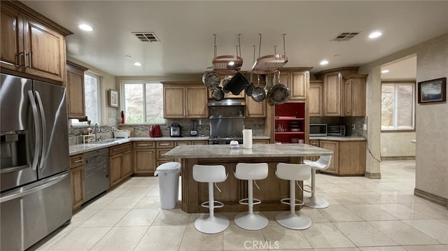 kitchen with a center island, stainless steel appliances, light stone counters, tasteful backsplash, and light tile flooring