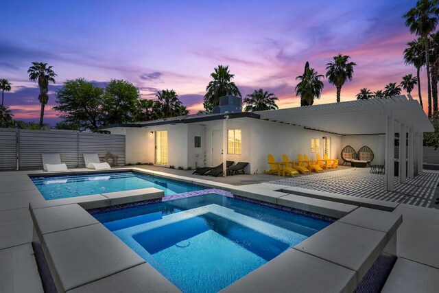 pool at dusk with a patio area and an in ground hot tub