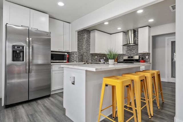 kitchen with white cabinetry, a center island, stainless steel appliances, wall chimney range hood, and a breakfast bar