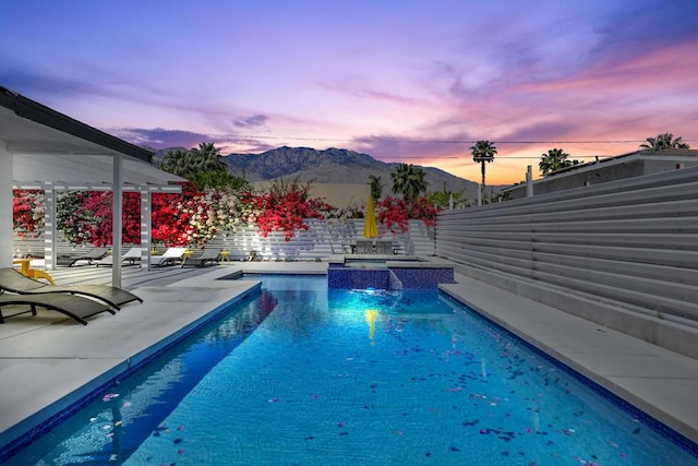 pool at dusk featuring a patio area, a mountain view, and an in ground hot tub