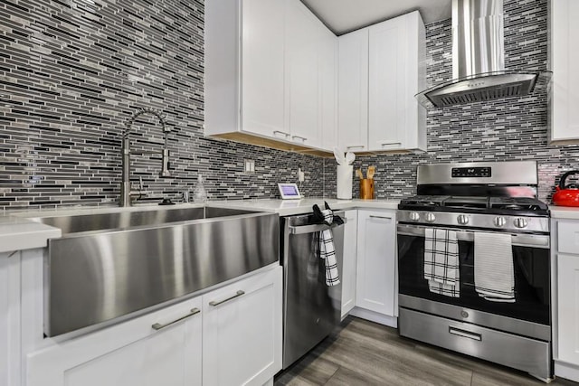 kitchen featuring appliances with stainless steel finishes, wall chimney exhaust hood, dark wood-type flooring, sink, and white cabinets