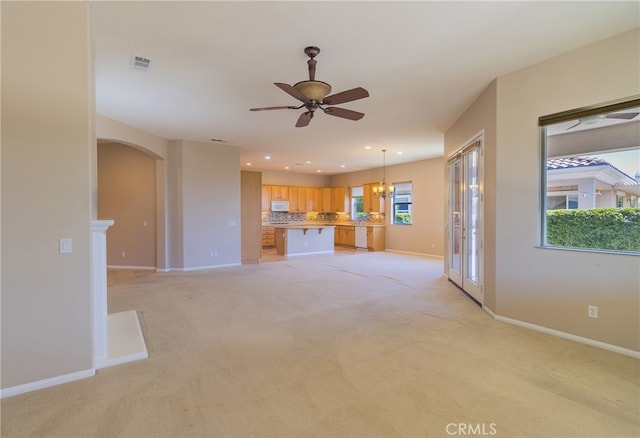 unfurnished living room featuring ceiling fan with notable chandelier, light colored carpet, and plenty of natural light