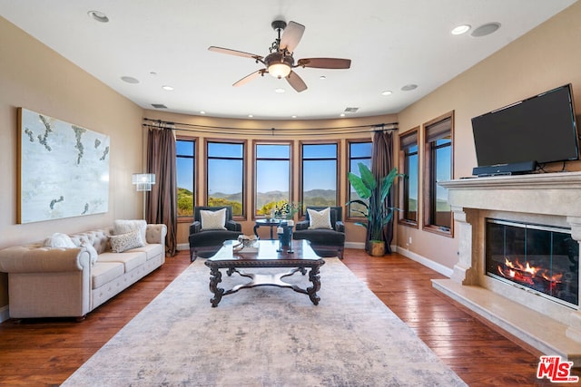 living room featuring ceiling fan, dark hardwood / wood-style flooring, and a premium fireplace