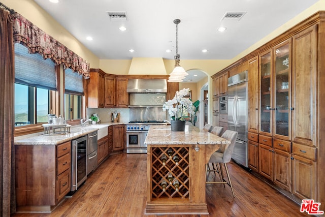 kitchen with premium appliances, tasteful backsplash, decorative light fixtures, wall chimney range hood, and a center island