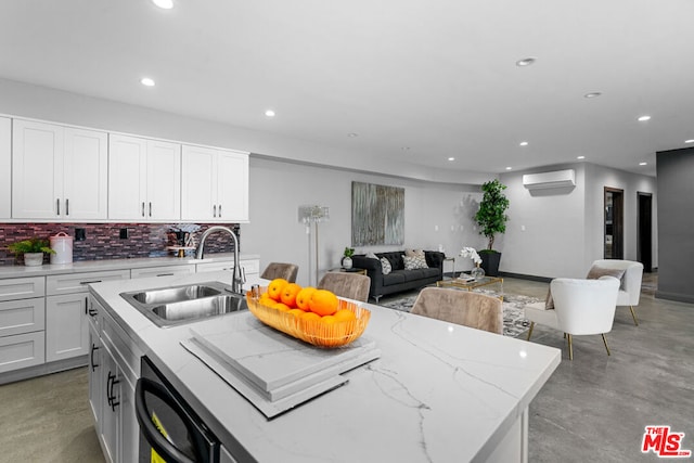 kitchen featuring a wall mounted AC, sink, white cabinetry, an island with sink, and dishwashing machine