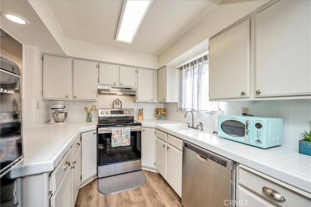 kitchen featuring sink, light hardwood / wood-style flooring, stainless steel appliances, tile counters, and white cabinets