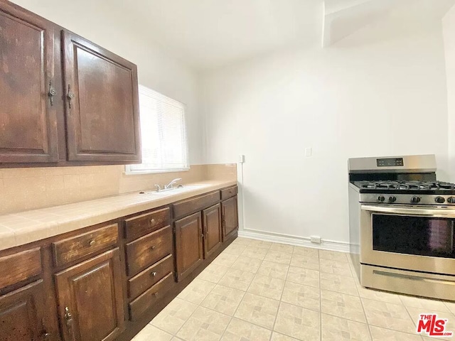 kitchen with sink, dark brown cabinets, stainless steel gas stove, and light tile flooring