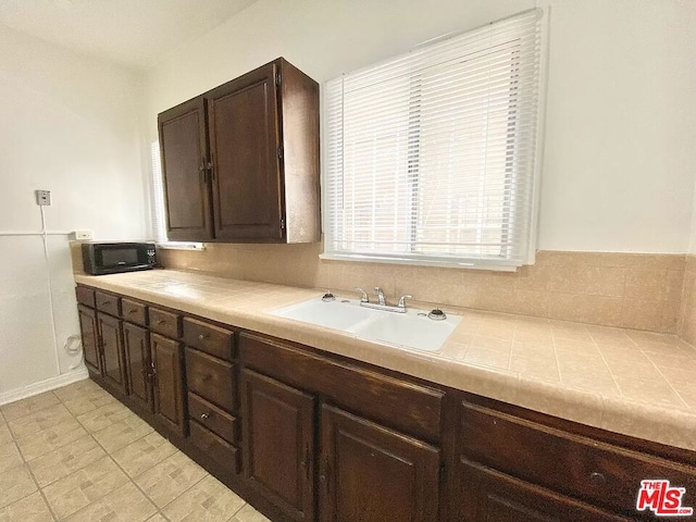 kitchen with dark brown cabinetry, sink, and light tile floors