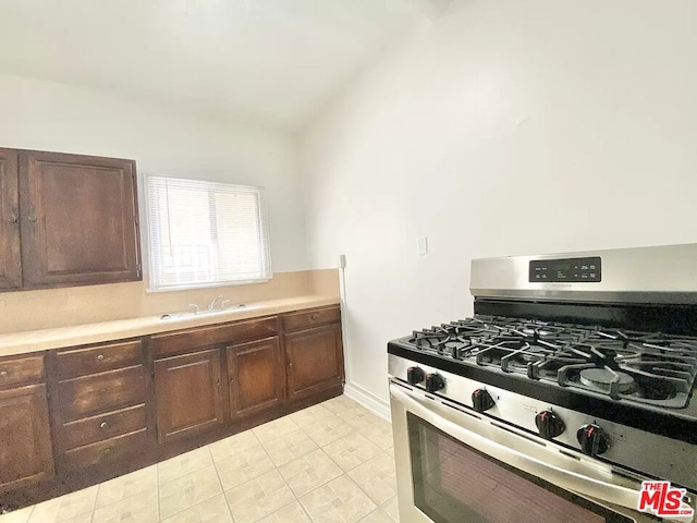 kitchen featuring dark brown cabinetry, sink, light tile floors, and range with gas stovetop