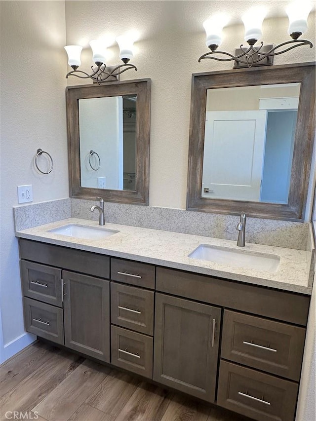 bathroom with a notable chandelier, dual vanity, and wood-type flooring