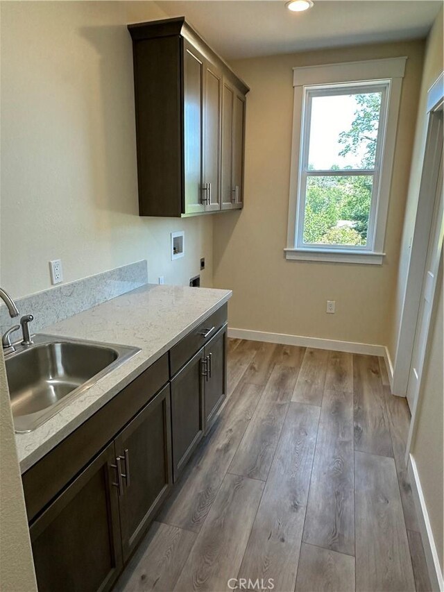 kitchen with sink, wood-type flooring, light stone countertops, and dark brown cabinetry