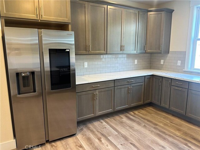 kitchen featuring stainless steel fridge with ice dispenser, backsplash, light hardwood / wood-style floors, and light stone counters