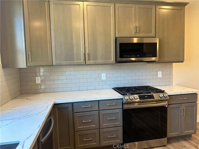 kitchen featuring backsplash, light stone counters, stainless steel appliances, and light hardwood / wood-style floors