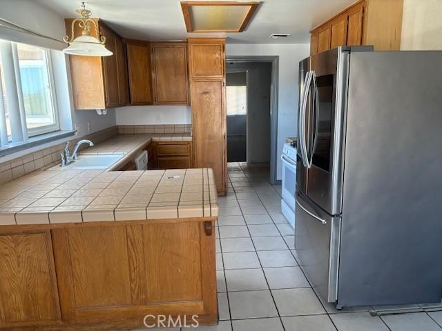 kitchen with a peninsula, a sink, brown cabinetry, tile counters, and smart refrigerator
