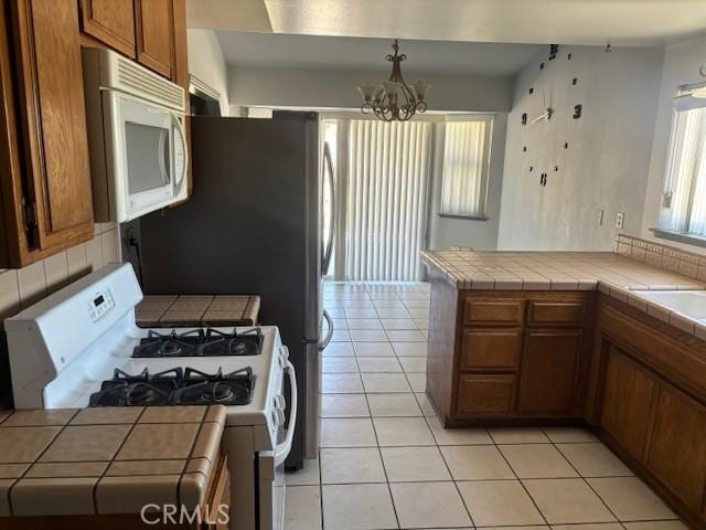 kitchen featuring brown cabinetry, white appliances, an inviting chandelier, and tile countertops
