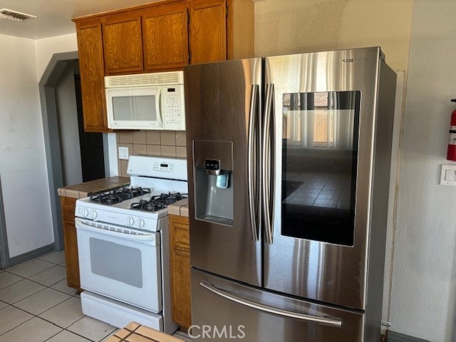 kitchen with white appliances, tile countertops, light tile patterned floors, and backsplash