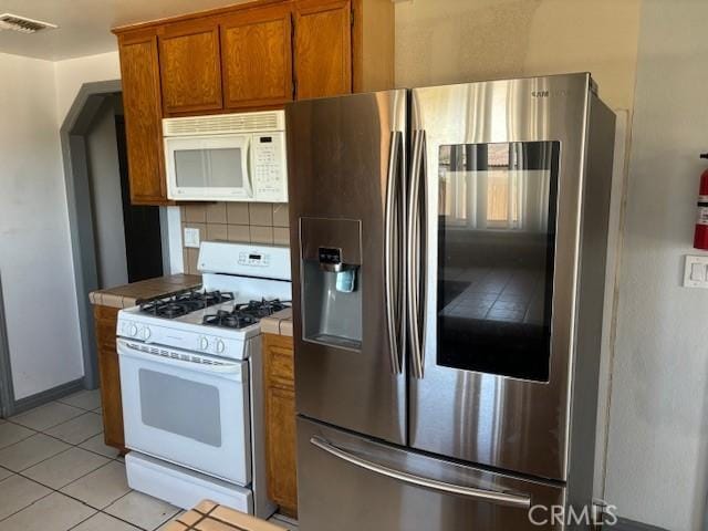 kitchen featuring light tile patterned floors, brown cabinets, tile counters, visible vents, and white appliances