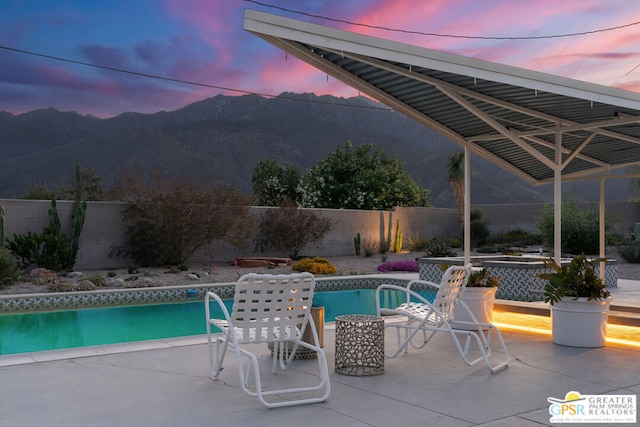 pool at dusk featuring a mountain view, a jacuzzi, and a patio area