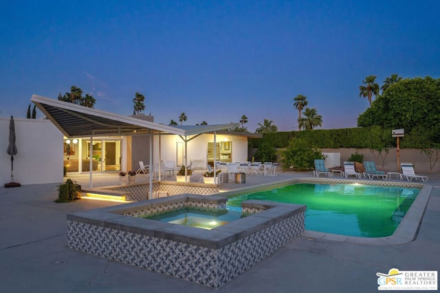 pool at dusk featuring an in ground hot tub and a patio area