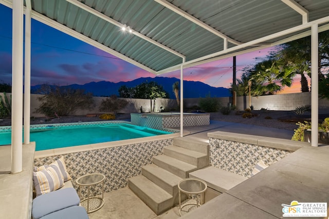 pool at dusk featuring a mountain view, a patio, and a jacuzzi