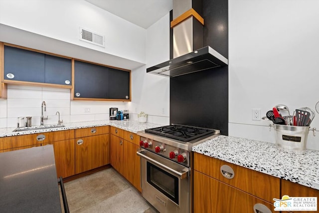 kitchen featuring wall chimney range hood, sink, light stone counters, and luxury range