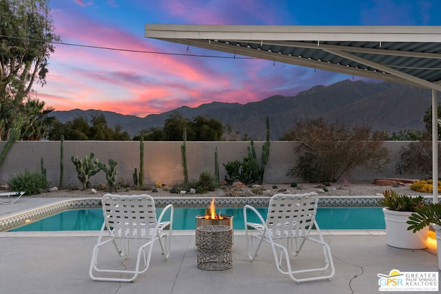 pool at dusk featuring a mountain view, a patio, and an outdoor fire pit