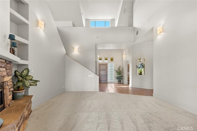 foyer entrance featuring arched walkways, a fireplace, light tile patterned floors, a towering ceiling, and light carpet