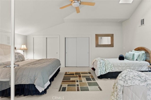 bedroom with visible vents, vaulted ceiling, carpet flooring, and two closets