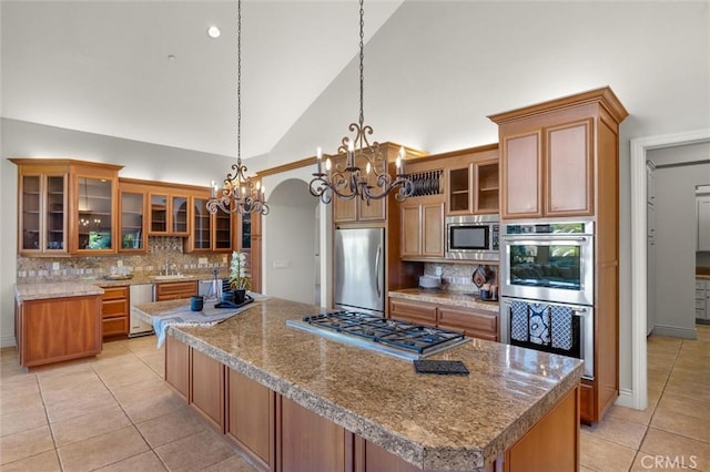 kitchen with appliances with stainless steel finishes, brown cabinetry, glass insert cabinets, and pendant lighting