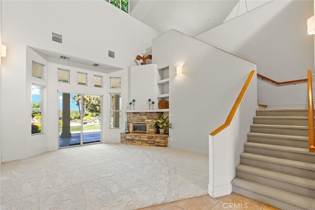 unfurnished living room with visible vents, stairway, a high ceiling, light carpet, and a stone fireplace