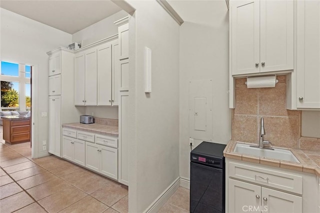 kitchen with tasteful backsplash, tile countertops, white cabinetry, a sink, and light tile patterned flooring