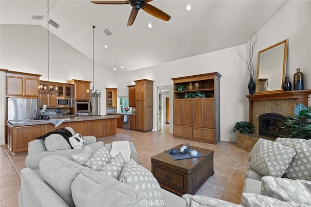 living room featuring a glass covered fireplace, light tile patterned flooring, visible vents, and ceiling fan with notable chandelier