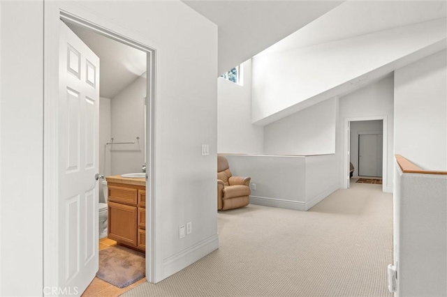 hall featuring an upstairs landing, baseboards, a sink, and light colored carpet