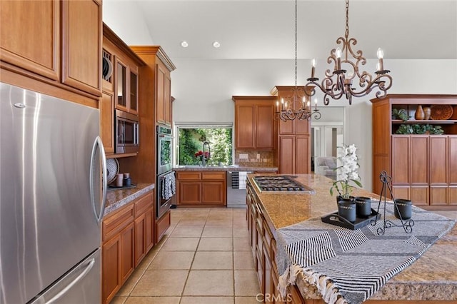 kitchen featuring light stone counters, stainless steel appliances, hanging light fixtures, backsplash, and brown cabinetry