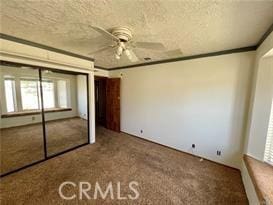 unfurnished bedroom featuring crown molding, carpet, ceiling fan, and a closet