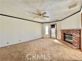 unfurnished living room featuring crown molding, a brick fireplace, carpet flooring, and ceiling fan