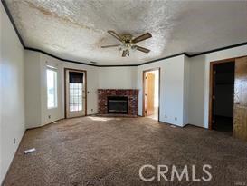 unfurnished living room featuring crown molding, a fireplace, ceiling fan, and carpet