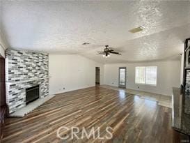 unfurnished living room featuring vaulted ceiling, a stone fireplace, dark hardwood / wood-style flooring, ceiling fan, and a textured ceiling