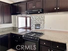 kitchen with dark brown cabinetry, extractor fan, a stone fireplace, and black appliances