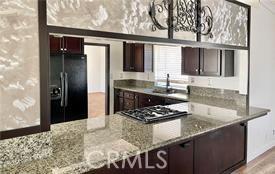 kitchen with dark brown cabinets, wood-type flooring, light stone countertops, black refrigerator with ice dispenser, and stainless steel gas stovetop