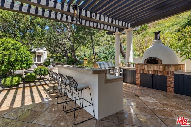 view of patio / terrace with exterior kitchen, exterior bar, grilling area, a pergola, and an outdoor brick fireplace