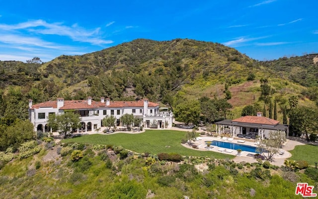 rear view of house featuring a balcony, a mountain view, a lawn, and a patio