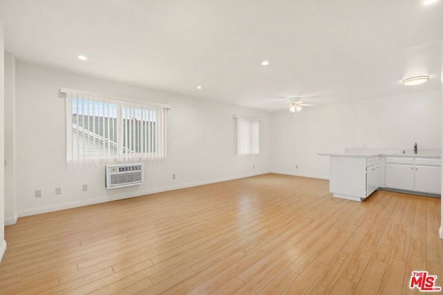 unfurnished room with light hardwood / wood-style flooring, a healthy amount of sunlight, ceiling fan, and a wall unit AC