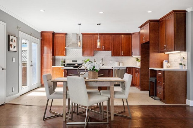 kitchen with hanging light fixtures, wall chimney range hood, tasteful backsplash, light hardwood / wood-style floors, and dishwasher