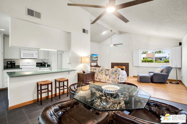 tiled living room featuring ceiling fan, a large fireplace, vaulted ceiling with beams, a textured ceiling, and sink