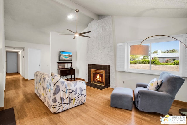 living room featuring ceiling fan, vaulted ceiling with beams, a fireplace, and light hardwood / wood-style flooring