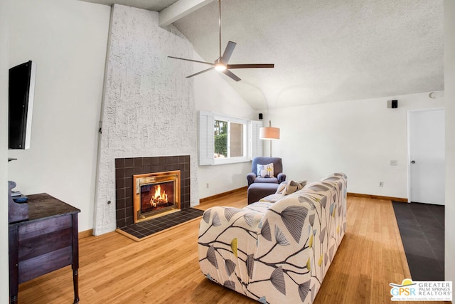 living room with ceiling fan, hardwood / wood-style floors, a tiled fireplace, and vaulted ceiling with beams