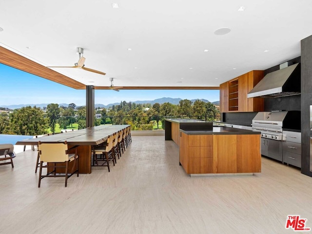 kitchen featuring ceiling fan, a kitchen island, wall chimney range hood, a breakfast bar area, and expansive windows